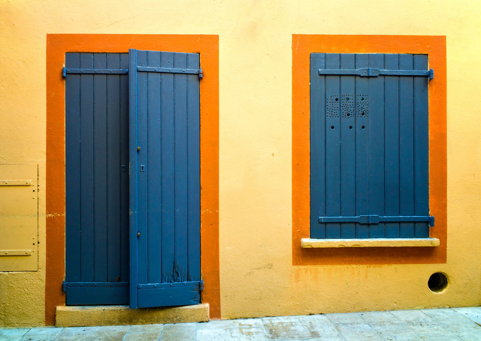 Closed blue shutters on a yellow and orange wall